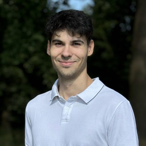 Portraitfoto von Haris Dedovic: freundlich lächelnder junger Mann mit dunklen Haaren im hellen Polohemd, im Freien vor grünem Hintergrund.